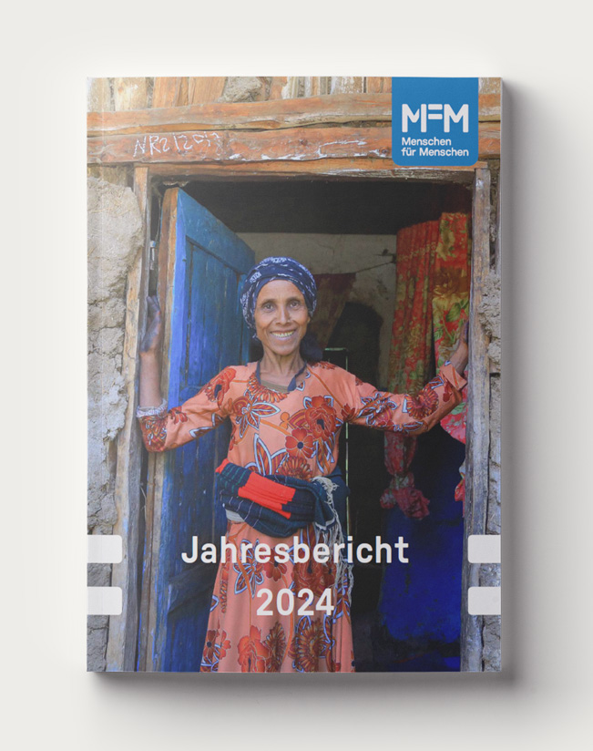Cover of the 2024 annual report showing a woman standing in the doorway of a wooden and mud house, smiling.