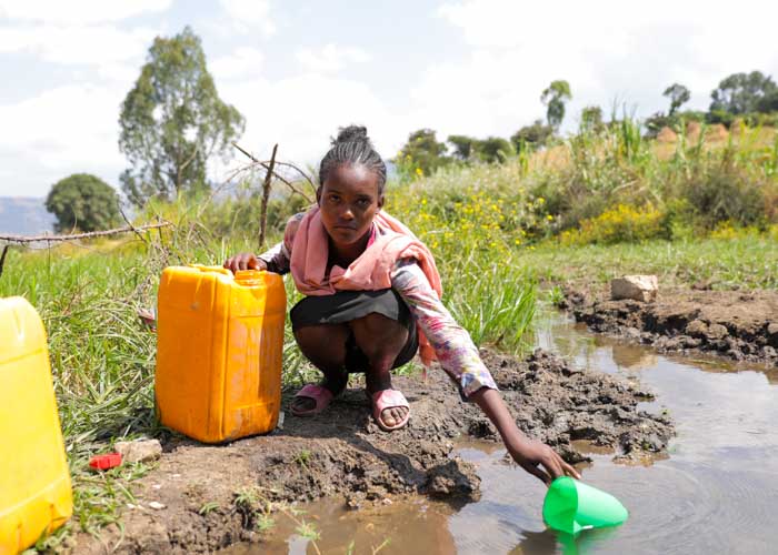 Mädchen in Äthiopien schöpft Wasser aus einer Pfütze