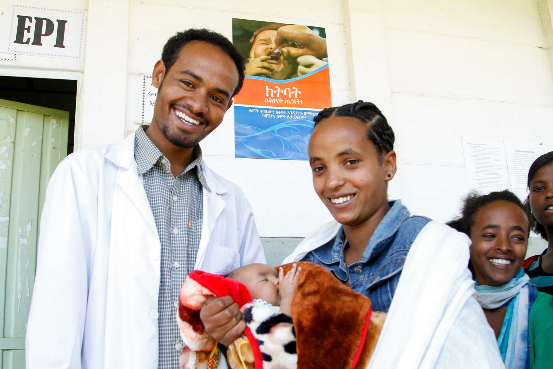 Doktor und Patientin lächeln in die Kamera mit Kind im Arm