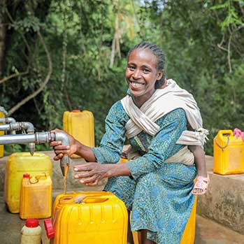Frau bei einer Quellfassung füllt sich sauberes Wasser in Kanister